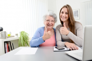 young woman helping old senior woman doing paperwork and administrative procedures with laptop computer at home